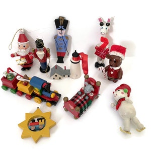 Op de afbeelding: Een verzameling kleurrijke kerstversieringen, waaronder een kerstman die op een trommel speelt, een soldaat, een trein, een beer met een kerstmuts, een giraffe met een sjaal, een muis op schaatsen en een ster met een trein.