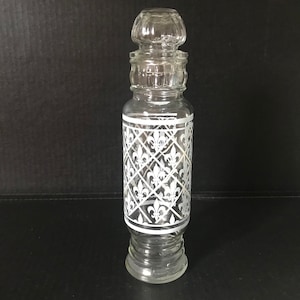 Peut inclure: Une bouteille en verre transparent avec un motif floral blanc. La bouteille a un couvercle décoratif avec un bouton sur le dessus.