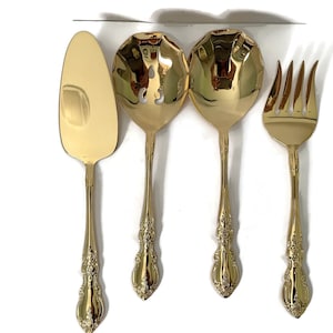 Puede incluir: Juego de cuatro utensilios de servicio chapados en oro, que incluyen un cuchillo para pastel, dos cucharas para servir y un tenedor para servir.