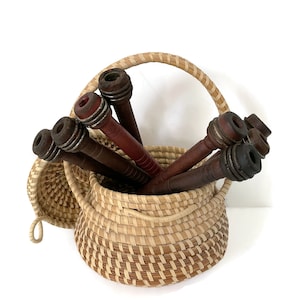 Puede incluir: Una cesta tejida con asa, llena de carretes de hilo de madera en tonos marrones y rojos.