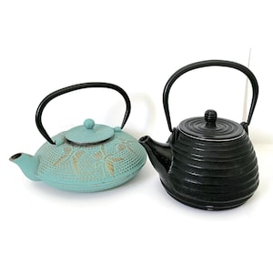 May include: Two cast iron teapots, one teal blue with a floral design and one black with a ribbed design.
