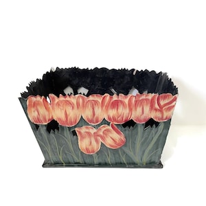 May include: A rectangular metal planter with a hand-painted tulip design. The planter features a dark gray base with green leaves and pink and red tulips. The top edge is scalloped and painted black.
