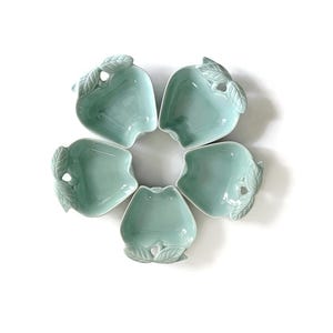 Könnte beinhalten: Fünf hellgrüne Keramikschalen in Apfelform, kreisförmig angeordnet. Jede Schale hat ein Blattdesign. Die Schalen befinden sich auf weißem Hintergrund.