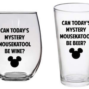 May include: Two clear glass drinkware items with black Mickey Mouse ears and text. The wine glass says "Can today's mystery mousekatool be wine?" and the beer glass says "Can today's mystery mousekatool be beer?"