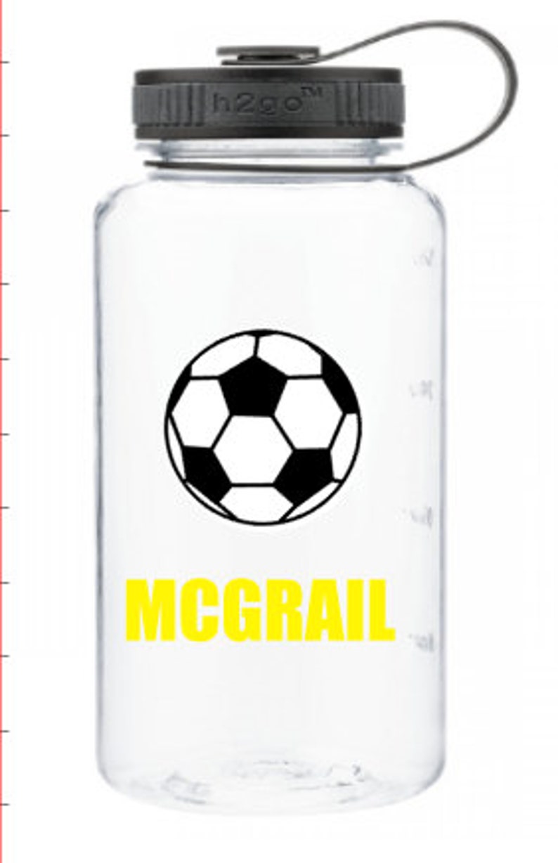 Puede incluir: Botella de agua de pl&aacute;stico transparente con tapa negra y un gr&aacute;fico de bal&oacute;n de f&uacute;tbol en blanco y negro. El nombre "MCGRAIL" est&aacute; impreso en amarillo debajo del gr&aacute;fico.