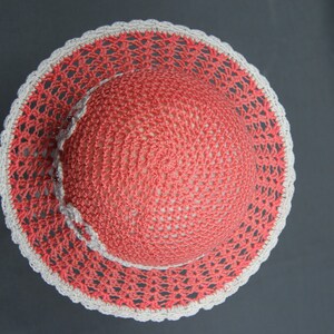 Puede incluir: Un sombrero de crochet con una corona de color rosa coral y un borde de crochet blanco.