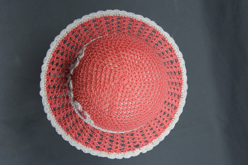 Puede incluir: Un sombrero de crochet con una corona de color rosa coral y un borde de crochet blanco.