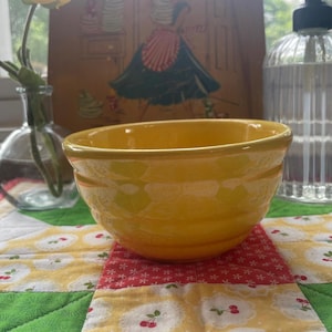 May include: A bright yellow ceramic mixing bowl with a smooth, glossy finish and three horizontal ridges encircling the exterior. The bowl features a wide, open top and a rounded base, showcasing a vibrant, solid color throughout its entire surface.