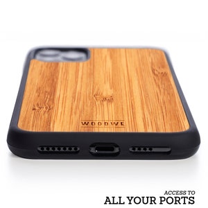 May include: A brown wood phone case with a black bumper. The case has the word "WOODWE" engraved on the back. The case has cutouts for the phone's camera, charging port, and buttons.