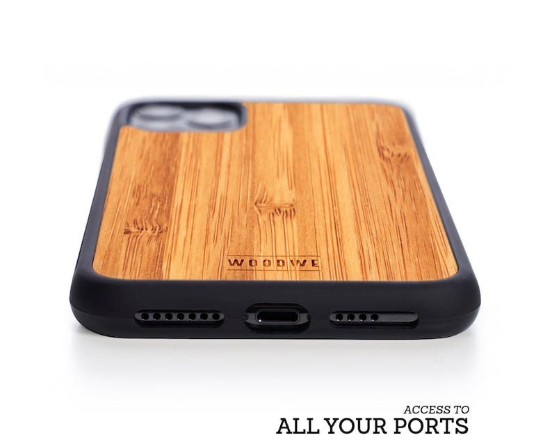 May include: A brown wood phone case with a black bumper. The case has the word "WOODWE" engraved on the back. The case has cutouts for the phone's camera, charging port, and buttons.