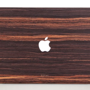 May include: A rectangular laptop skin featuring a dark brown and black wood grain pattern with horizontal stripes. A white Apple logo is centered on the surface, and the word WOODWE is printed in small letters near the bottom center.