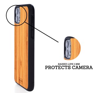 May include: A brown wood phone case with a black border and a raised lip around the camera lens. The case is made of bamboo and has a natural wood grain. The text "RAISED LIPS 1 MM PROTECTS CAMERA" is printed on the case.