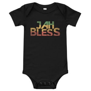 Puede incluir: Body de bebé negro con la frase "JAH BLESS" en una fuente multicolor desgastada. El texto es verde, amarillo y rojo, que recuerda a la bandera rastafari. El body tiene mangas cortas y corchetes en la parte inferior.