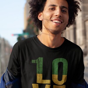 May include: A black t-shirt featuring a graphic of the word "LOVE" in red, yellow and green. The letters are styled to look like wood.