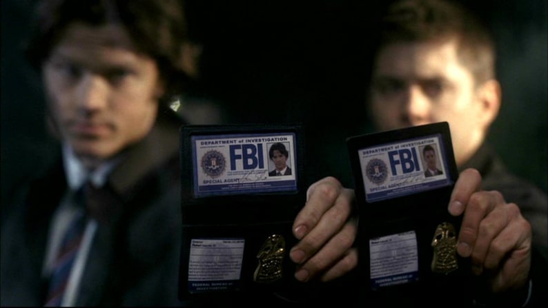 May include: Two men are holding up FBI badges. The badges are black with a blue and white design. The text on the badges reads "Department of Investigation FBI Special Agent".
