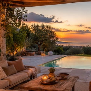 Puede incluir: Una tranquila escena al aire libre al atardecer, con una piscina y una zona de estar. Una mesa de centro de madera con una vela y plantas se encuentra frente a un sofá beige con cojines marrones. El cielo es naranja y amarillo.