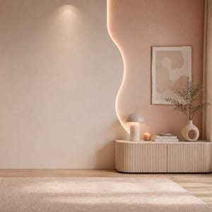 May include: A beige fluted sideboard sits against a curved wall with integrated warm lighting. On the sideboard, a mushroom-shaped lamp, a lit candle, a stack of books, and a white ceramic vase with a leafy branch are displayed below wall art.