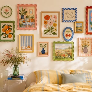 Puede incluir: Una pared de galería con varias láminas enmarcadas, incluyendo ilustraciones botánicas, paisajes y bodegones con marcos coloridos ondulados y rectos, sobre una cama con ropa de cama a rayas amarillas y un jarrón de cristal verde.