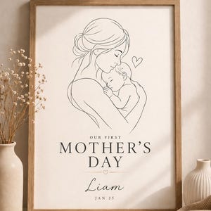 Puede incluir: Un grabado enmarcado en madera con un dibujo lineal de una madre abrazando a un bebé, con el texto "OUR FIRST MOTHER'S DAY" y un nombre y una fecha. La obra de arte es en blanco y negro sobre un fondo crema.