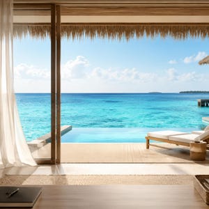 May include: A view from an indoor space looking out toward a turquoise ocean and a clear blue sky. A wooden deck features a white lounge chair and a small cylindrical side table. A thatched roof overhangs the outdoor area, and a sheer curtain hangs.