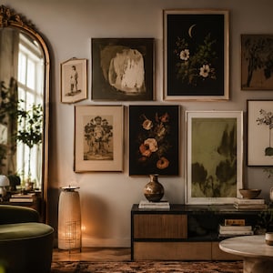 Op de afbeelding: Een galerijmuur met zeven ingelijste kunstprints in verschillende formaten, waaronder botanische illustraties, abstracte vormen en een halve maan. Een hoge gouden boogspiegel, een cilindrische vloerlamp en een lage houten kast zijn aanwezig.