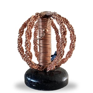 Peut inclure: Une sculpture en fil de cuivre avec une base ronde. Le fil est enroulé en forme de sphère avec plusieurs couches. La sculpture est sur une base en bois noir.