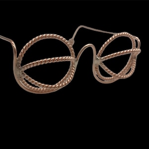 May include: Eyeglasses with a distinctive design. The frames are crafted from a twisted, rope-like material in a copper hue. The lenses are circular, and the arms are slender and straight. The background is black.