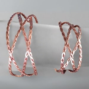 May include: Two rose gold braided copper bracelets. The bracelets are made of woven copper wire and are designed to be adjustable.