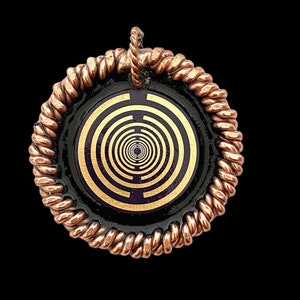 May include: A copper wire wrapped pendant with a black background and a gold spiral design. The pendant features a circular design with a concentric circle pattern.