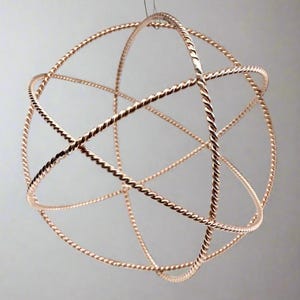 Puede incluir: Una escultura esférica de color cobre compuesta por varillas de metal retorcidas e entrelazadas. El diseño geométrico crea un orbe abierto tridimensional, suspendido por un fino alambre. El metal tiene un acabado pulido.