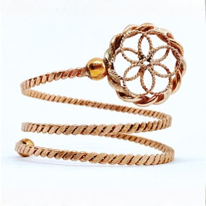 May include: A gold-toned spiral bracelet with a floral design. The bracelet wraps around the wrist with a twisted rope design. The floral element is a circular openwork design. The bracelet has a small gold ball at each end.