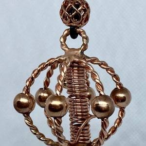 May include: A copper wire sculpture necklace with a spiral design and multiple small copper spheres. The necklace is suspended from a black leather cord with a decorative copper bead.