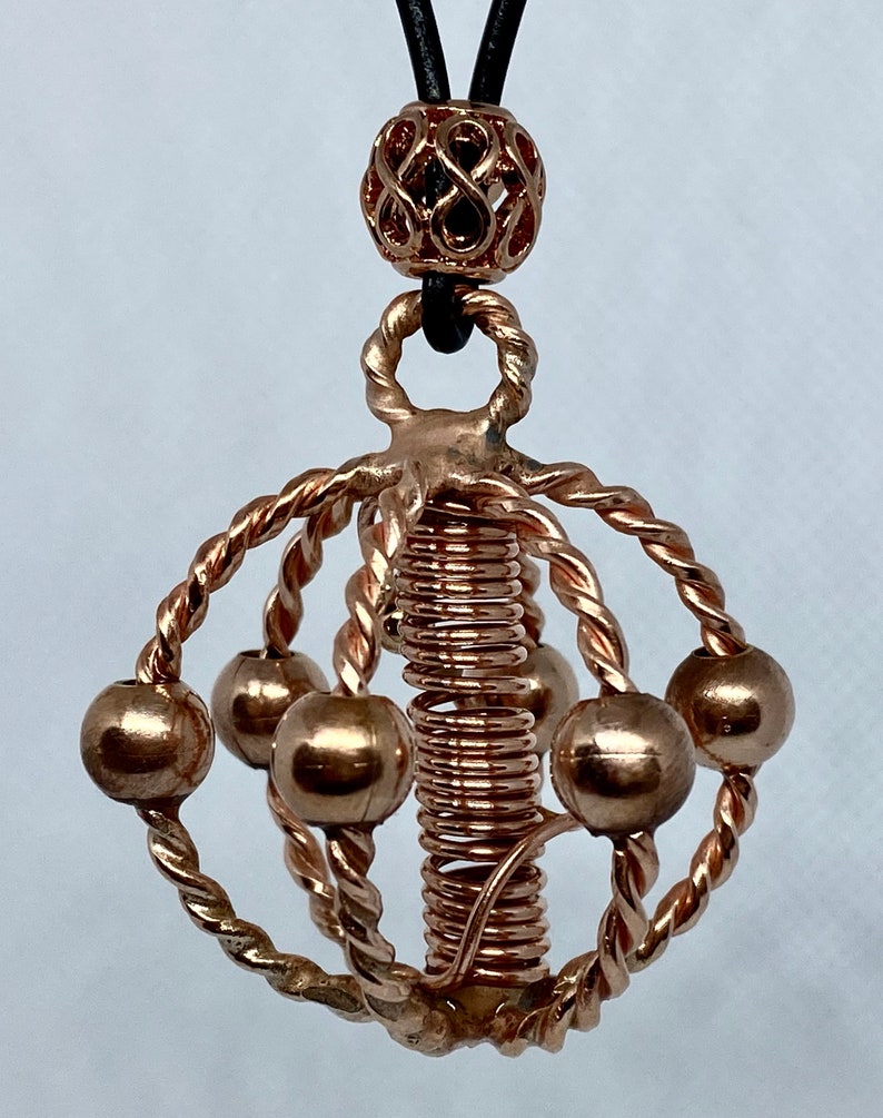 May include: A copper wire sculpture necklace with a spiral design and multiple small copper spheres. The necklace is suspended from a black leather cord with a decorative copper bead.