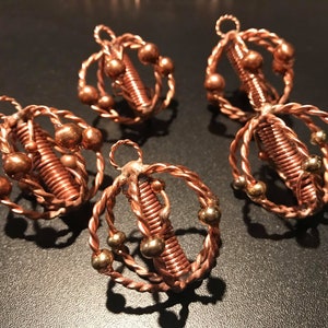 May include: Four copper wire ornaments with a spiral design and copper and gold beads. The ornaments are hanging from a dark surface.