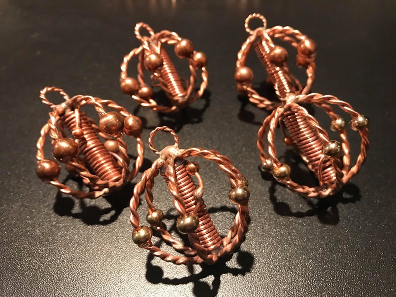 May include: Four copper wire ornaments with a spiral design and copper and gold beads. The ornaments are hanging from a dark surface.