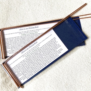 May include: Copper divining rods with instructions on a blue card. The rods are L-shaped, with one end straight and the other bent. The card has text about using the rods for dowsing, a method of finding underground water or minerals.