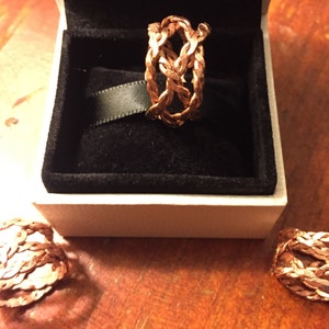 May include: Three rose gold braided rings in a white box. The rings are made of a woven metal design.