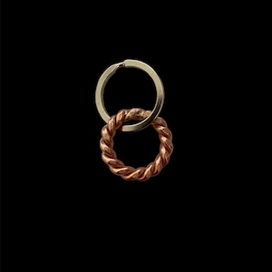 Puede incluir: Un llavero de plata con un anillo de cobre trenzado unido a él.