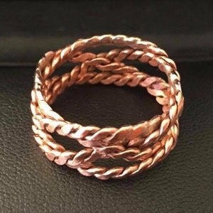 May include: A copper ring with a braided design. The ring is made of three strands of copper wire that are woven together.