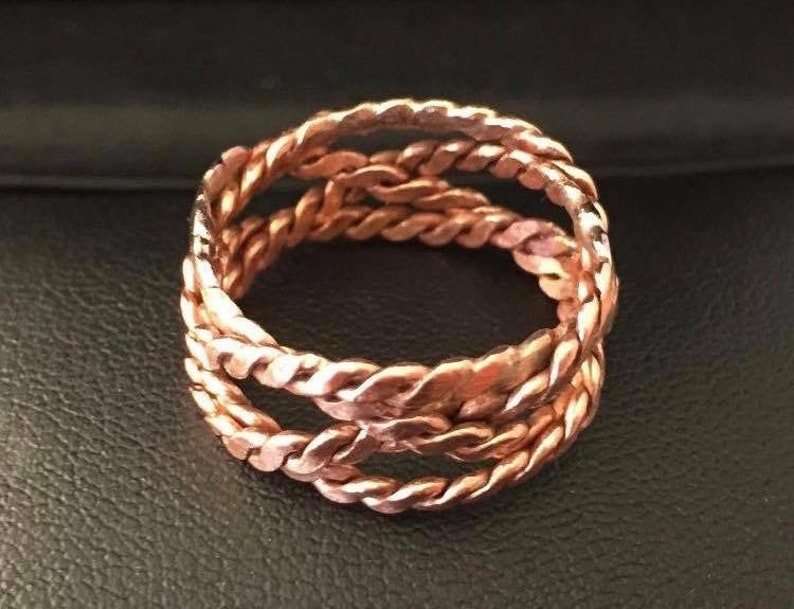 May include: A copper ring with a braided design. The ring is made of three strands of copper wire that are woven together.