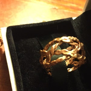 May include: Two gold-toned braided rings in a black velvet box. The rings are made of multiple strands of braided metal.
