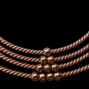 Op de afbeelding: Een koperen ketting met een gedraaid touwontwerp en een cluster van koperen kralen in het midden.