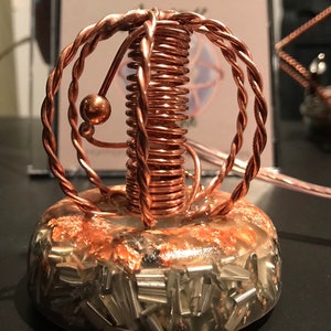May include: A copper wire sculpture with a sphere shape, a coil, and a small copper ball. The sculpture is on a clear base with copper flakes and silver metal pieces.