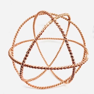 May include: A copper-colored, geometric sphere sculpture. The sphere is constructed from twisted wire, forming a series of interconnected, rounded shapes. The sculpture is displayed against a white background, highlighting its intricate design and metallic sheen.