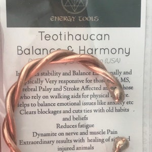 Può includere: Un braccialetto in filo di rame con un design intrecciato. Il braccialetto è su una carta bianca con il testo "Teotihaucan Balance & Harmony" e "Sacred Knowledge Energy Tools".