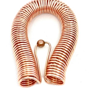 May include: A copper coil bracelet with a small ball at the top. The bracelet is made of multiple coils of copper wire.