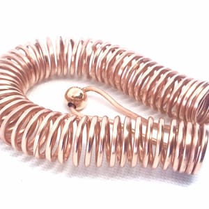May include: A rose gold colored metal coil bracelet with a small ball at the end of the clasp.