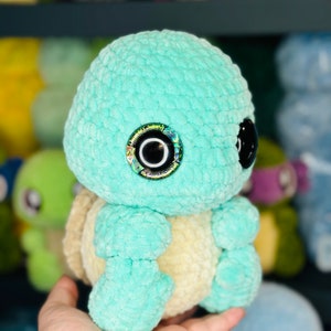May include: A crocheted turquoise turtle plush toy with a yellow shell and iridescent eyes.