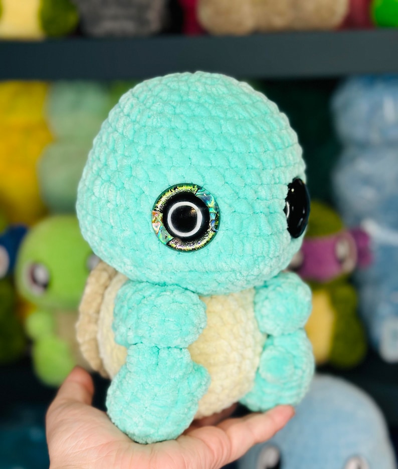 Pu&ograve; includere: Un giocattolo di peluche di tartaruga color turchese lavorato a uncinetto con un guscio giallo e occhi iridescenti.