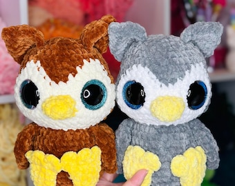 Op de afbeelding: Twee gehaakte uil knuffels, een bruin met gele accenten en een grijs met gele accenten. Beide uilen hebben grote, glinsterende blauwe ogen.